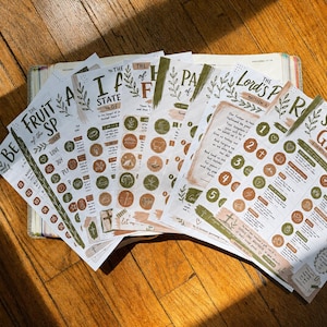May include: A collection of white paper sheets featuring printed religious text and circular icons in shades of olive green and terracotta. The pages include headings such as The Fruit of the Spirit, The Lord's Prayer, and Spiritual Gifts with botanical illustrations.