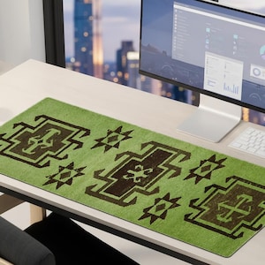 May include: A rectangular green desk mat with a geometric brown pattern. The mat is placed on a light-colored desk, with a computer monitor, keyboard, and mouse visible. The design features repeating shapes.
