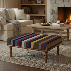 May include: A rectangular ottoman with a multi-colored striped top in shades of blue, red, yellow, and green. The ottoman has a wooden frame and legs. The room features a fireplace, sofa, and rug.