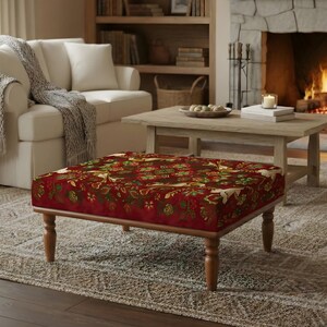 May include: A rectangular ottoman with a red floral pattern and wooden legs. The ottoman is in a living room setting with a white sofa, a wooden coffee table, and a fireplace.
