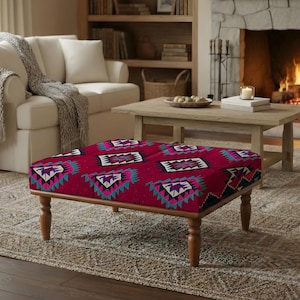 Może przedstawiać: Kwadratowa pufa z żywym czerwonym materiałem z geometrycznym wzorem w kolorze turkusowym, fioletowym i białym. Pufa ma drewnianą ramę i nogi, dodając ciepła do salonu. Wymiary: około 91 cm x 91 cm.