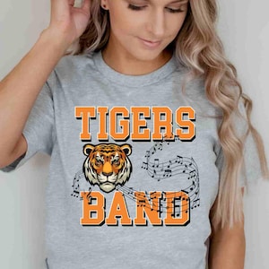 May include: A gray t-shirt with the words "TIGERS BAND" in orange block letters. A tiger's face is centered below the word "TIGERS". Musical notes are above and below the word "BAND".