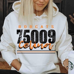 May include: A white hooded sweatshirt with the word "BOBCATS" in orange block letters above the number "75009" in black. Below the number is the word "Celina" in orange script. Two orange stripes are below the word Celina.