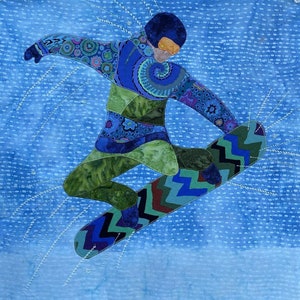 May include: A fabric art piece depicting a snowboarder in mid-air. The figure is clad in a blue and green patterned outfit, with a blue helmet and orange goggles. The snowboarder is on a blue background with white stitched lines.