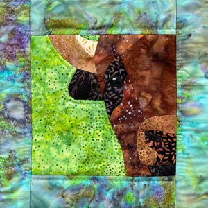 May include: A close-up of a quilt block featuring a brown and white patchwork bull's head against a green background with white polka dots. The bull's head is made of various fabric scraps sewn together.