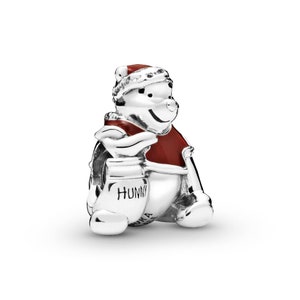 May include: Silver charm featuring Winnie the Pooh wearing a red Santa hat and holding a honey pot. The charm has red enamel detailing and the words "Hunny" on the pot.