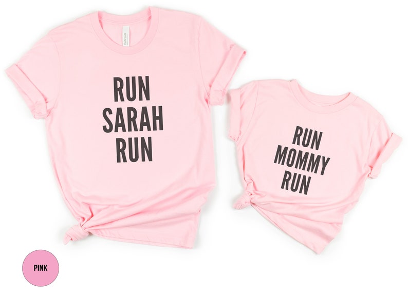 May include: Two pink t-shirts with black text. The larger shirt says "Run Sarah Run". The smaller shirt says "Run Mommy Run".