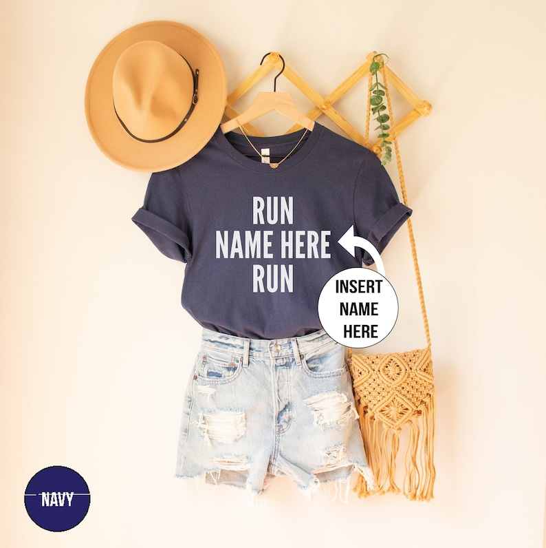 May include: Navy blue t-shirt with the text "RUN NAME HERE RUN" in white. The text "INSERT NAME HERE" is in a circle on the right side of the shirt.