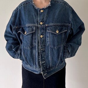 May include: A blue denim jacket with a frayed collar and gold buttons. The jacket has a relaxed fit and is cropped at the waist.