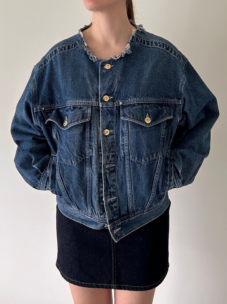May include: A blue denim jacket with a frayed collar and gold buttons. The jacket has a relaxed fit and is cropped at the waist.