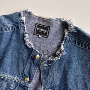 May include: A blue denim jacket with a frayed collar and a black label that reads "VERSACE JEANS COUTURE".