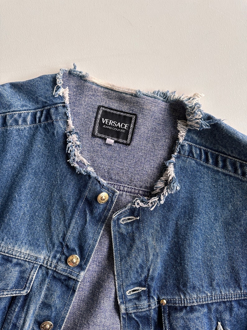May include: A blue denim jacket with a frayed collar and a black label that reads "VERSACE JEANS COUTURE".
