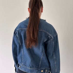 May include: A blue denim jacket with a slightly oversized fit. The jacket has a button closure and a frayed collar.