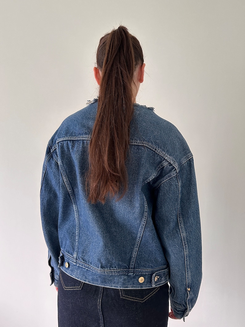May include: A blue denim jacket with a slightly oversized fit. The jacket has a button closure and a frayed collar.