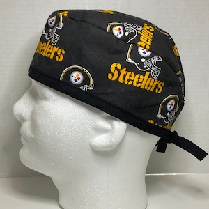 Könnte beinhalten: Schwarze OP-Mütze mit einem sich wiederholenden Muster aus gelben und schwarzen Pittsburgh Steelers-Logos. Die Mütze hat einen schwarzen Gummizug am Hinterkopf.