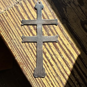 May include: A silver cross pendant with intricate floral designs. The cross has four arms and is decorated with a repeating pattern.