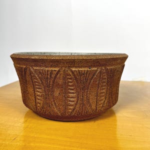 Op de afbeelding: Een bruine keramische kom met een witte rand en een geometrisch patroon. De kom staat op een houten oppervlak.