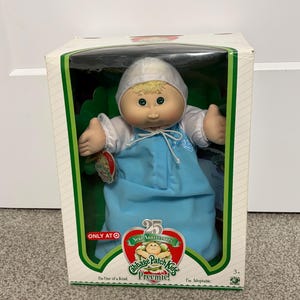 May include: A Cabbage Patch Kids Preemie doll in its original box. The doll has blonde hair and is wearing a blue outfit and a white bonnet. The box has a green border and text that reads "25 Year Anniversary" and "Only at Target."