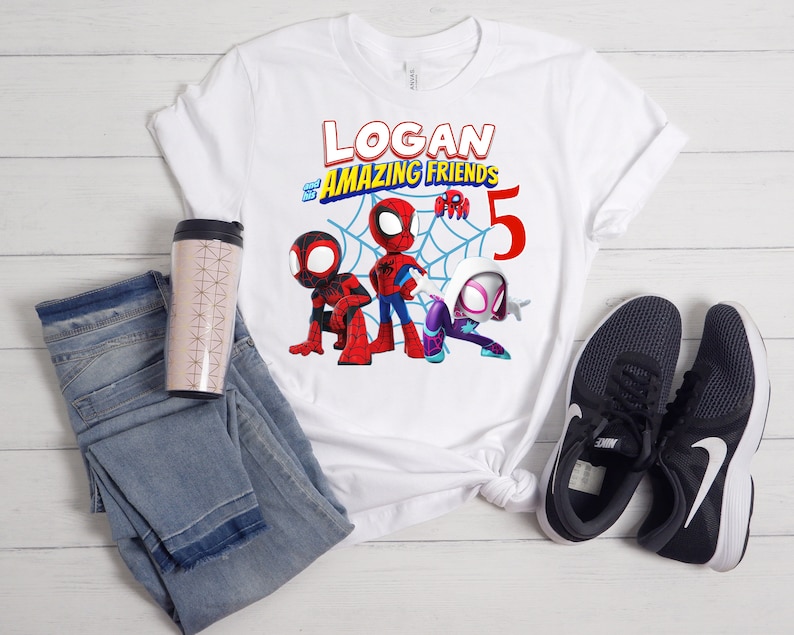 以下が含まれることがあります： スパイダーマンのキャラクターと「LOGAN and his AMAZING FRIENDS 5」の文字が描かれた、カラフルなグラフィックの白いTシャツ。デザインには、スパイダーマン、マイルズ・モラレス、スパイダーグウェンが含まれています。シャツは、青いジーンズ、トラベルマグ、黒いスニーカーと組み合わせています。