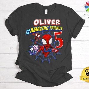 Pode incluir: Uma t-shirt preta de manga curta com uma impress&atilde;o gr&aacute;fica de tr&ecirc;s personagens com tema de aranha sobre uma teia de aranha azul. O texto diz OLIVER and his AMAZING FRIENDS com um grande n&uacute;mero 5 vermelho. Design em vermelho, azul e branco.