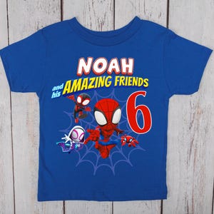 Pode incluir: Uma t-shirt de manga curta azul-real com uma impress&atilde;o gr&aacute;fica contendo o texto NOAH and his AMAZING FRIENDS, um n&uacute;mero 6 grande em vermelho e ilustra&ccedil;&otilde;es de tr&ecirc;s personagens animados sobre um design de teia de aranha azul-escuro.