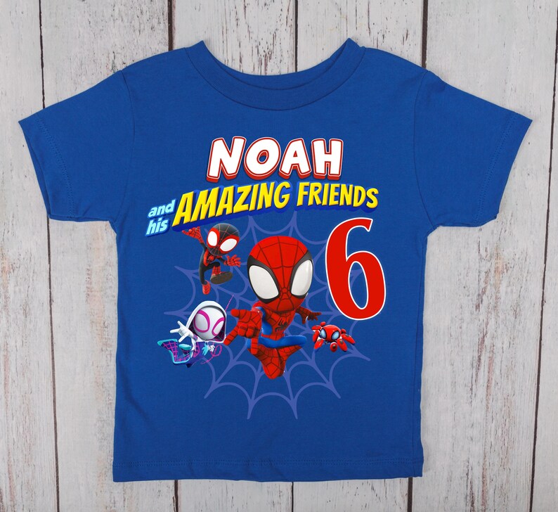 Pode incluir: Uma t-shirt de manga curta azul-real com uma impress&atilde;o gr&aacute;fica contendo o texto NOAH and his AMAZING FRIENDS, um n&uacute;mero 6 grande em vermelho e ilustra&ccedil;&otilde;es de tr&ecirc;s personagens animados sobre um design de teia de aranha azul-escuro.