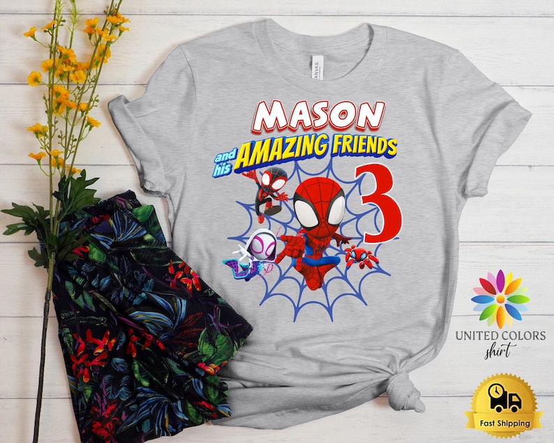 Pode incluir: Uma t-shirt cinzenta clara de manga curta com uma impress&atilde;o gr&aacute;fica com o texto MASON and his AMAZING FRIENDS e um grande n&uacute;mero 3 vermelho. O design inclui personagens de desenhos animados em vermelho, azul e branco sobre uma teia.