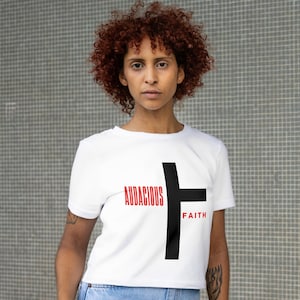 May include: White cropped t-shirt with a black cross graphic and the text "Audacious Faith" in red.