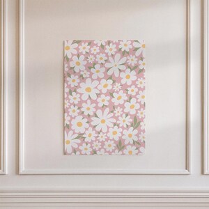 Peut inclure: Une impression murale rectangulaire présentant un motif répétitif de marguerites blanches à cœur jaune et de petites feuilles vertes sur un fond rose clair uni. Le motif floral recouvre toute la surface de l'impression verticale.
