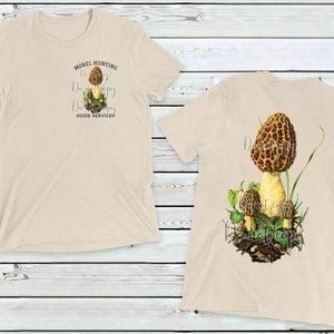 May include: Two beige t-shirts with a mushroom design. The front shirt has the text "Morel Hunting Don't Worry Be Happy Guide Services". The back shirt has a large illustration of a morel mushroom.