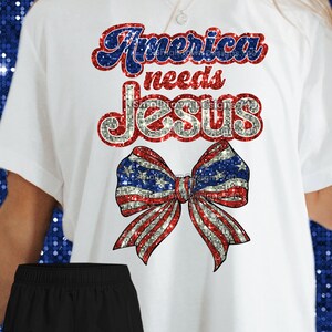 May include: White t-shirt with a red, white, and blue glitter bow and the text "America needs Jesus".