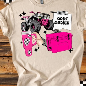 May include: Beige t-shirt featuring a pink ATV with a black and white checkered design, a pink cooler, and a pink tumbler. The text "GOIN' MUDDIN'" is displayed on a white background. Black stars and checkered patterns complete the design.