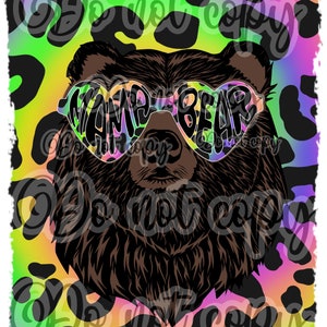 May include: A brown bear wearing heart-shaped sunglasses with the text "Mama Bear" on them. The bear is on a background of black and yellow leopard print with a rainbow gradient.