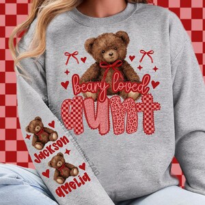 May include: A gray sweatshirt with a teddy bear graphic and the words "beary loved aunt". The design includes red hearts, bows, and the names "Jackson" and "Amelia" on the sleeve. The teddy bear has a red bow.