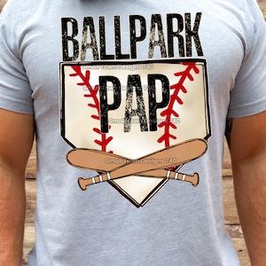May include: A gray t-shirt with a baseball-themed graphic. The graphic features a baseball diamond with a baseball bat and ball, and the text "BALLPARK PAP".