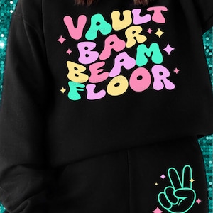 Puede incluir: Sudadera negra con las palabras "VAULT BAR BEAM FLOOR" en letras de burbuja de colores. La sudadera tiene un signo de paz en el bolsillo.