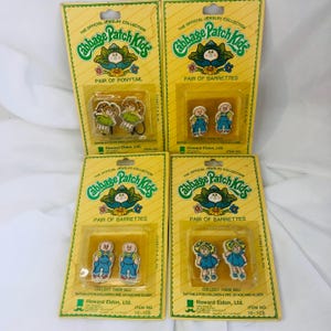 Könnte beinhalten: Vier Vintage Cabbage Patch Kids Schmucksets auf gelben Karten. Zwei Sets sind Haarspangenpaare, und eines ist ein Paar Haargummis. Die Karten tragen den Text "The Official Jewelry Collection" und "Collect Them All!"