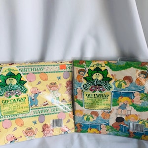 Peut inclure: Deux rouleaux de papier cadeau Cabbage Patch Kids. L'un a un fond jaune avec des illustrations de Cabbage Patch Kids, des ballons et les mots "Happy Birthday". L'autre a un fond vert clair avec des Cabbage Patch Kids dans une piscine.