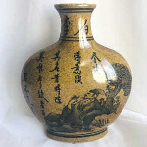 May include: A tan ceramic vase with black calligraphy and a painted scene of a man under a tree. The vase has a rounded body, a narrow neck, and a dark blue rim and base. The calligraphy is in Chinese characters.
