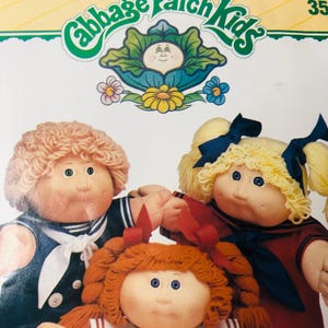 May include: Image of Cabbage Patch Kids dolls. The dolls have soft, round faces, and yarn hair in various colours. They are wearing sailor-style outfits with red and blue accents. The Cabbage Patch Kids logo is at the top.