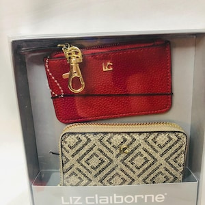 Może przedstawiać: Czerwony skórzany etui na karty ze złotym zapięciem i wzorzysty portfel są prezentowane w przezroczystym pudełku. Etui na karty ma złote inicjały "LC". Portfel ma geometryczny wzór i złoty zamek błyskawiczny.