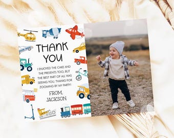 May include: A thank you card with a colorful illustration of various vehicles, including a truck, a train, a helicopter, a car, and a scooter. The card has a photo of a young boy in a white shirt and black pants, and the text "Thank You" in black lettering. The text below the photo reads "I enjoyed the cake and the presents too, but the best part of all was seeing you. Thanks for zooming by my party! From, Jackson."