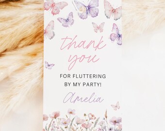 May include: A white gift tag with a string, featuring watercolor butterflies in pink and purple. The tag reads "thank you" in cursive, with the text "FOR FLUTTERING BY MY PARTY! Amelia" below, and a floral border.