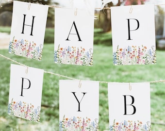 May include: A banner spelling "HAPPY" with individual white cards. Each card has a black letter and a watercolor floral border in shades of purple, yellow, and blue. The banner is strung on a twine line with a blurred outdoor background.