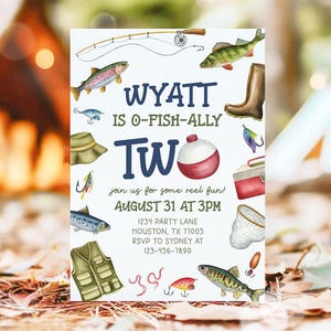 May include: A white birthday invitation with a blue and white 'Two' in the center. The invitation features a fishing theme with illustrations of fish, fishing rods, a tackle box, and a fishing net. The text reads 'Wyatt is O-Fish-Ally Two' and 'Join us for some reel fun! August 31 at 3PM'. The invitation also includes the address '1234 Party Lane, Houston, TX 77005' and the RSVP information 'RSVP to Sydney at 123-456-7890'.