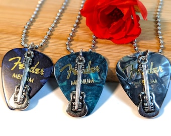 May include: Three guitar pick necklaces with silver ball chains. Each pick has a Fender logo and a silver guitar charm. The picks are blue, teal, and gray, with the word "MEDIUM" printed on them.