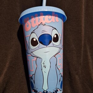 Puede incluir: Vaso de pl&aacute;stico azul claro con el personaje Stitch de la pel&iacute;cula de Disney Lilo & Stitch. El vaso tiene una tapa y una pajita azules a juego. La palabra "Stitch" est&aacute; impresa en rosa en el lateral del vaso.