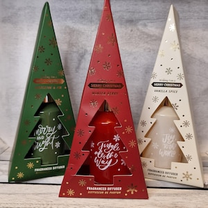 May include: Three triangular fragrance diffuser boxes in green, red, and cream. The green box reads Mistletoe & Fir and Merry and Bright. The red box reads Winter Berry and Jingle all the Way. The cream box reads Vanilla Spice and Joy to the World.