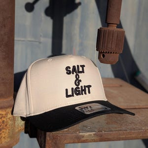 May include: A white and black baseball cap with the text "SALT & LIGHT" embroidered in black on the front.