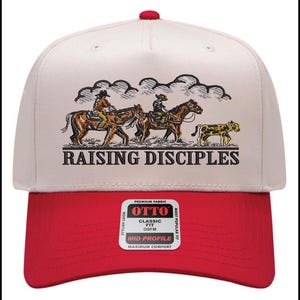 Puede incluir: Gorra de b&eacute;isbol con visera roja y corona crema. La gorra presenta una ilustraci&oacute;n de personas a caballo y el texto "RAISING DISCIPLES". La gorra tiene un ajuste cl&aacute;sico y un perfil medio.